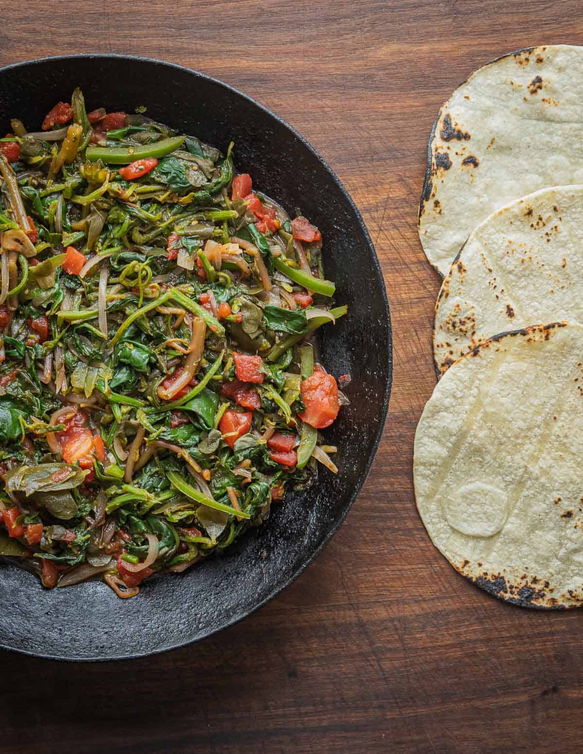 A pan of cooked quelites guisadas next to grilled tortillas.