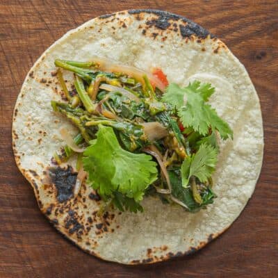 A grilled tortilla filled with cooked greens and cilantro.