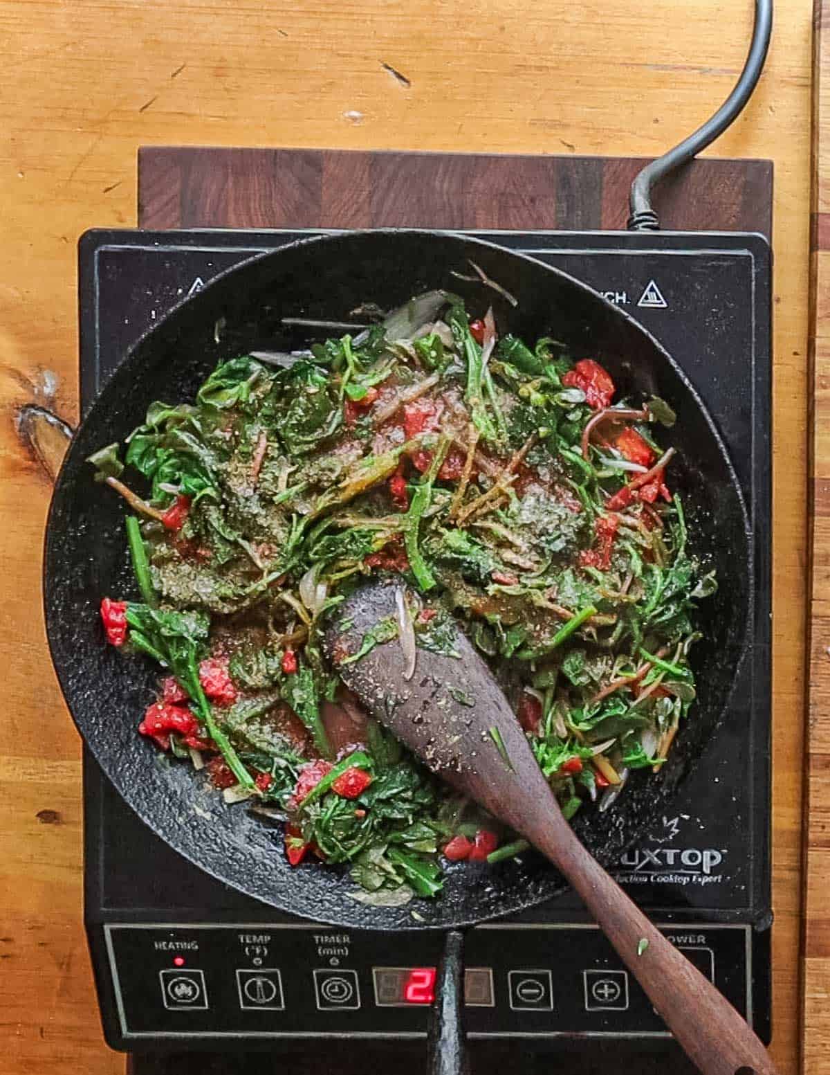 Adding greens and chopped tomatoes to a pan of cooked shallots and jalapeno.