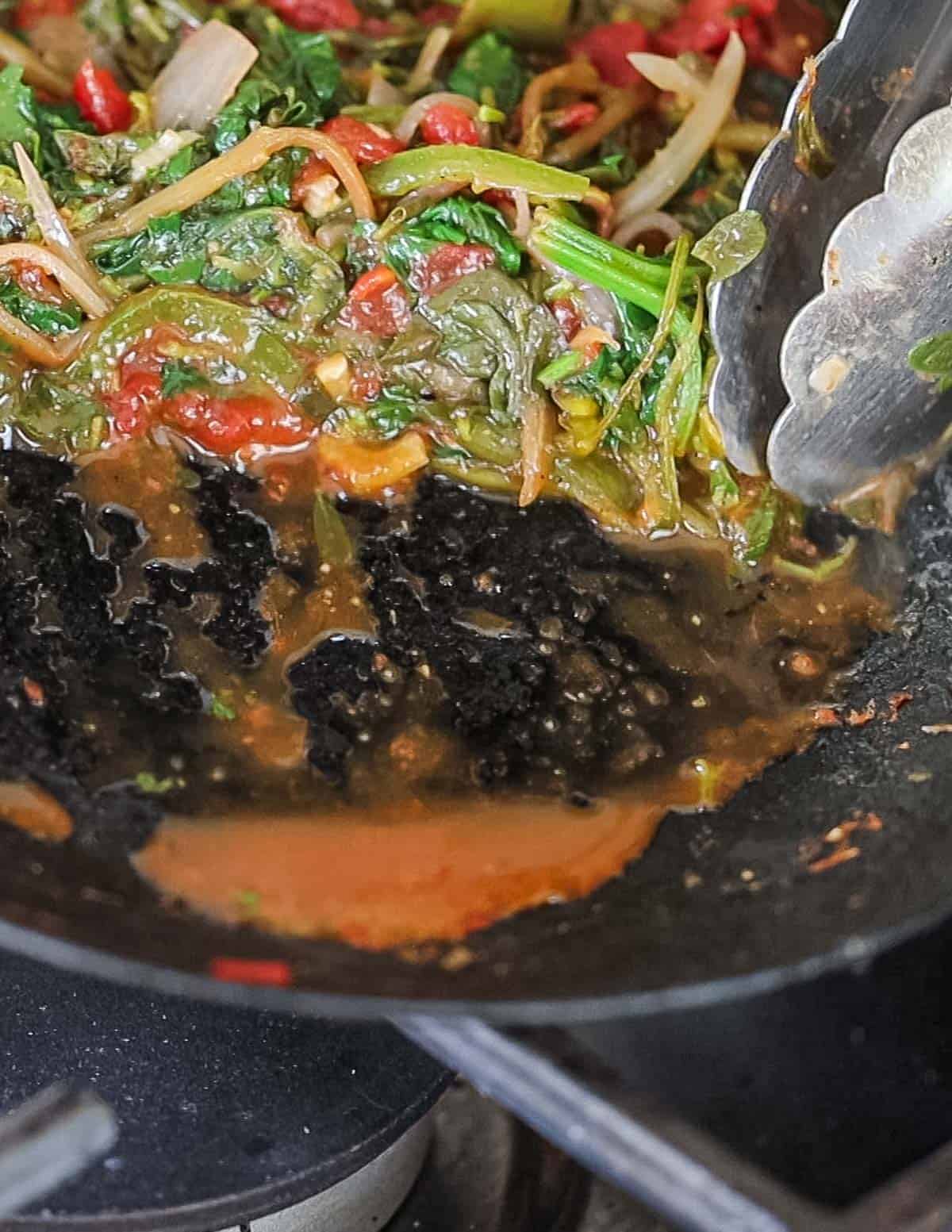 A close up image of a pan of cooked greens showing juices running in the bottom of the pan. 