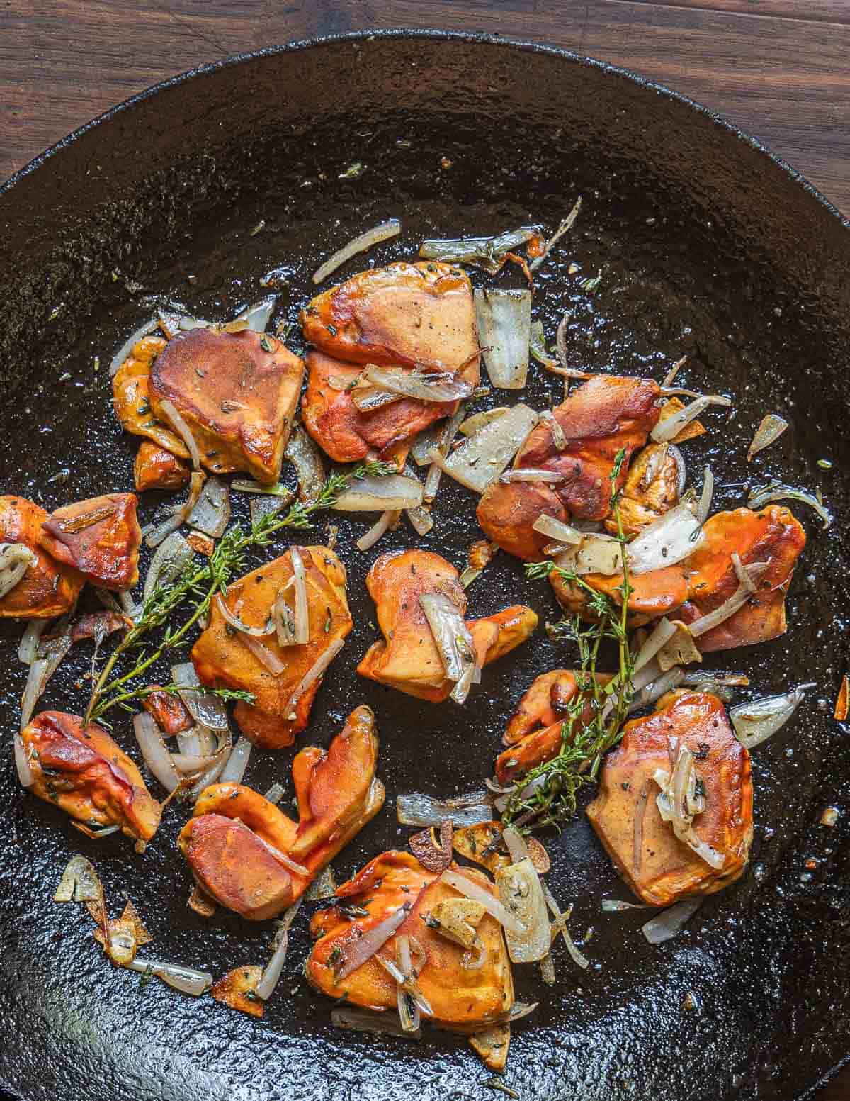 A close up image of orange chicken mushrooms cooking in a pan with garlic, shallots and fresh thyme sprigs. 