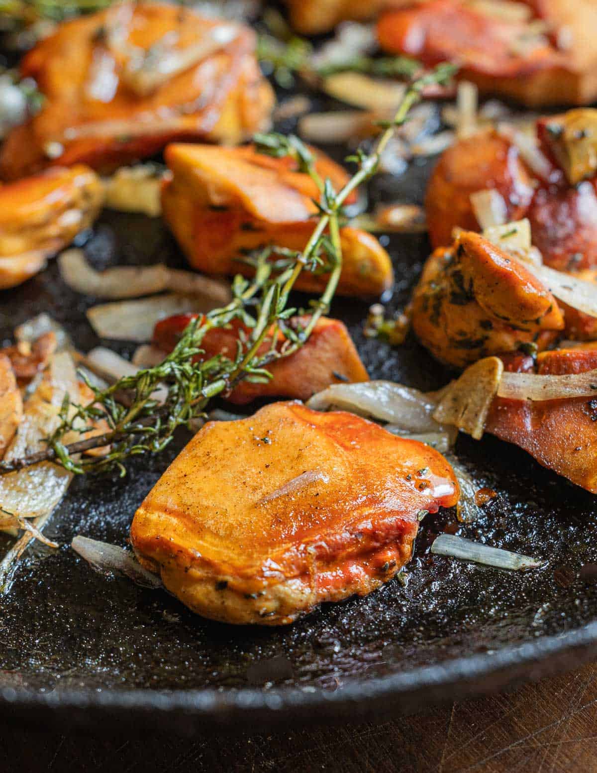 A close up image of chicken of the woods mushrooms cooking in a pan with shallots, garlic and thyme sprigs. 