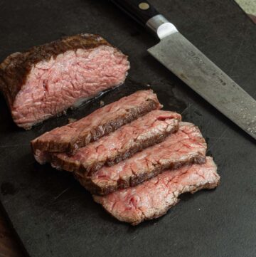 A sliced, medium rare bavette steak on a cutting board.