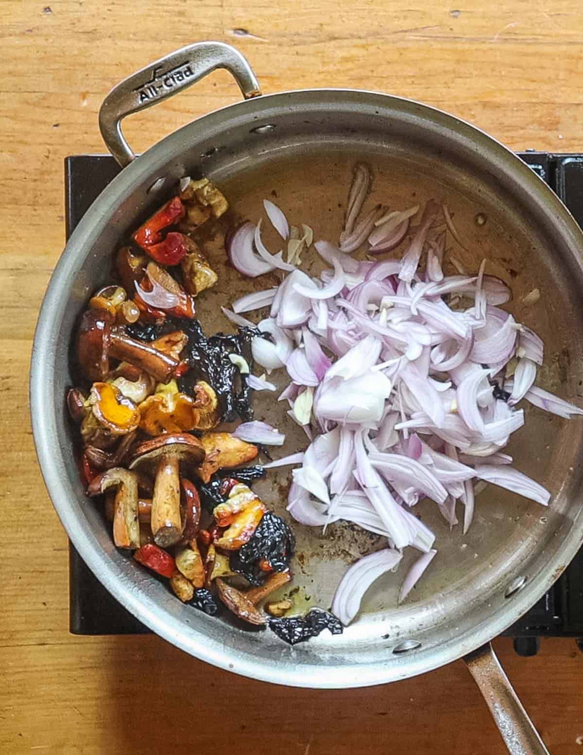 Adding shallots to a pan of wild mushrooms cooking. 