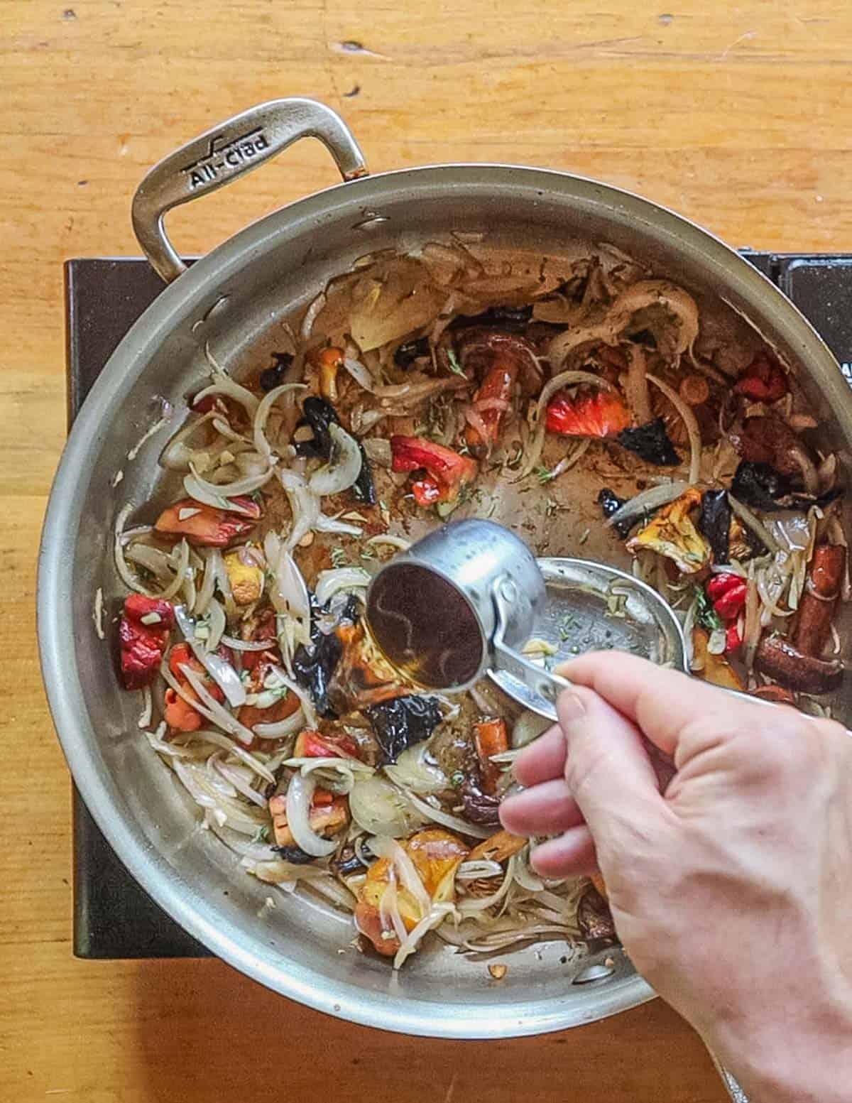 Adding brandy to a pan of cooked wild mushrooms and shallots. 