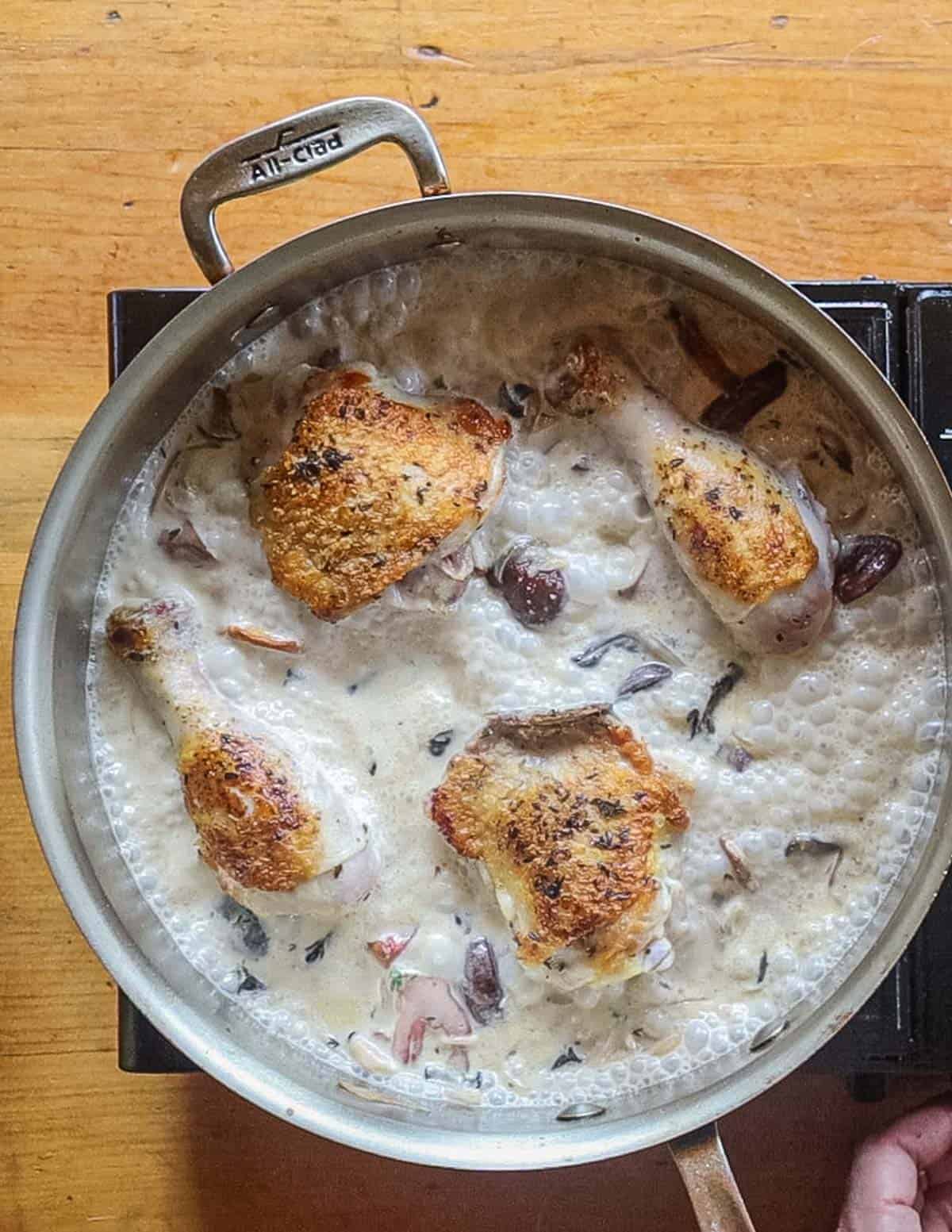 Browned chicken legs and thighs cooking in a mushroom sauce. 