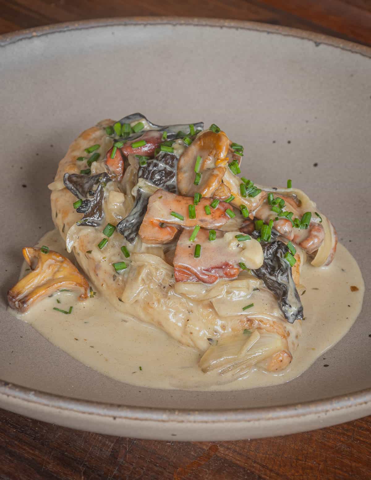 Chicken on a plate covered in mushroom sauce garnished with chives. 