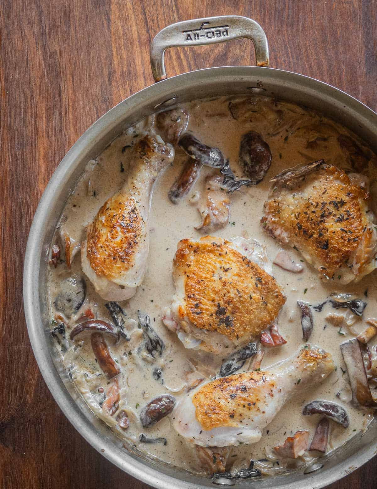 Chicken legs and thighs with golden brown skin cooking in a wild mushroom sauce. 