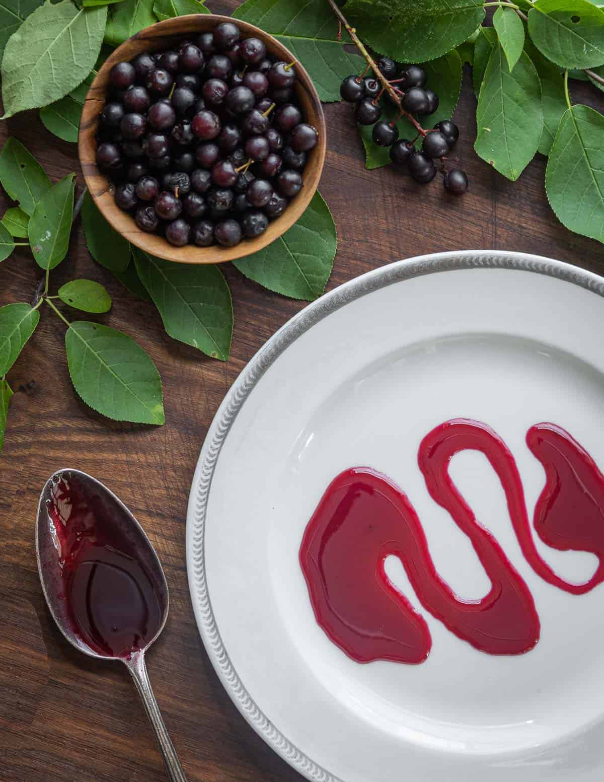 Chokecherry syrup on a plate surrounded by cherry leaves and wild cherries. 