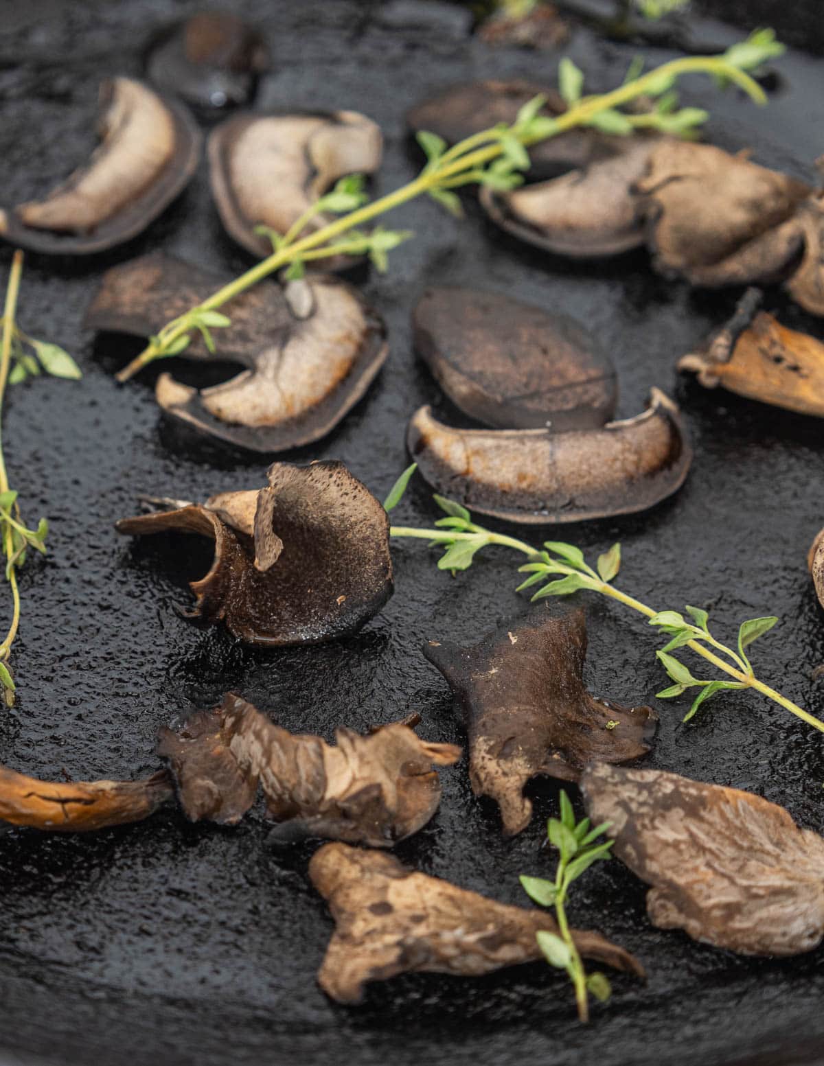 Black velvet bolete mushrooms cooking in a pan with black trumpet mushrooms. 