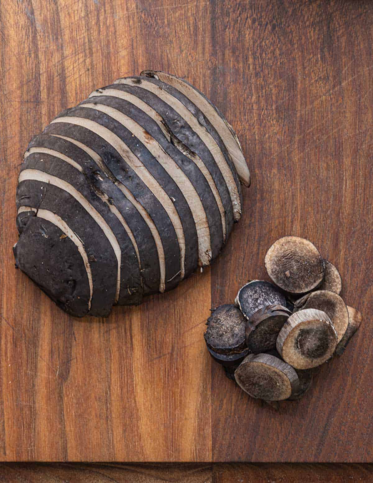 A sliced black mushroom cap next to sliced stems. 