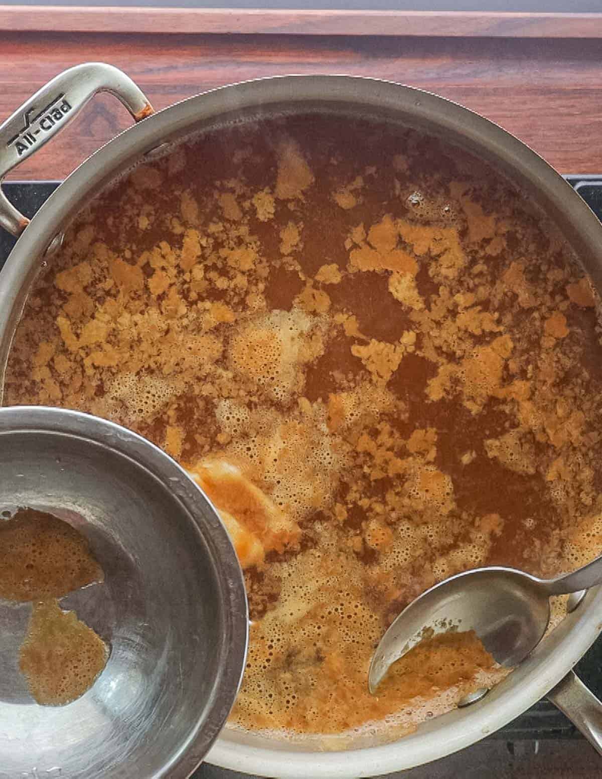 Skimming impurities from a pan of cooking apple cider. 