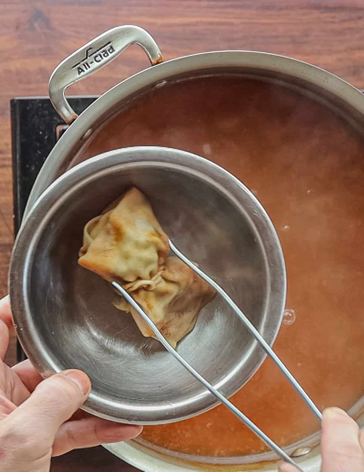 Removing a spice bouquet from a pan with culinary tweezers. 