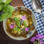 A top down view of a bowl of ciambotta or giambotta Italian vegetable stew garnished with basil sprigs and phlox flowers.