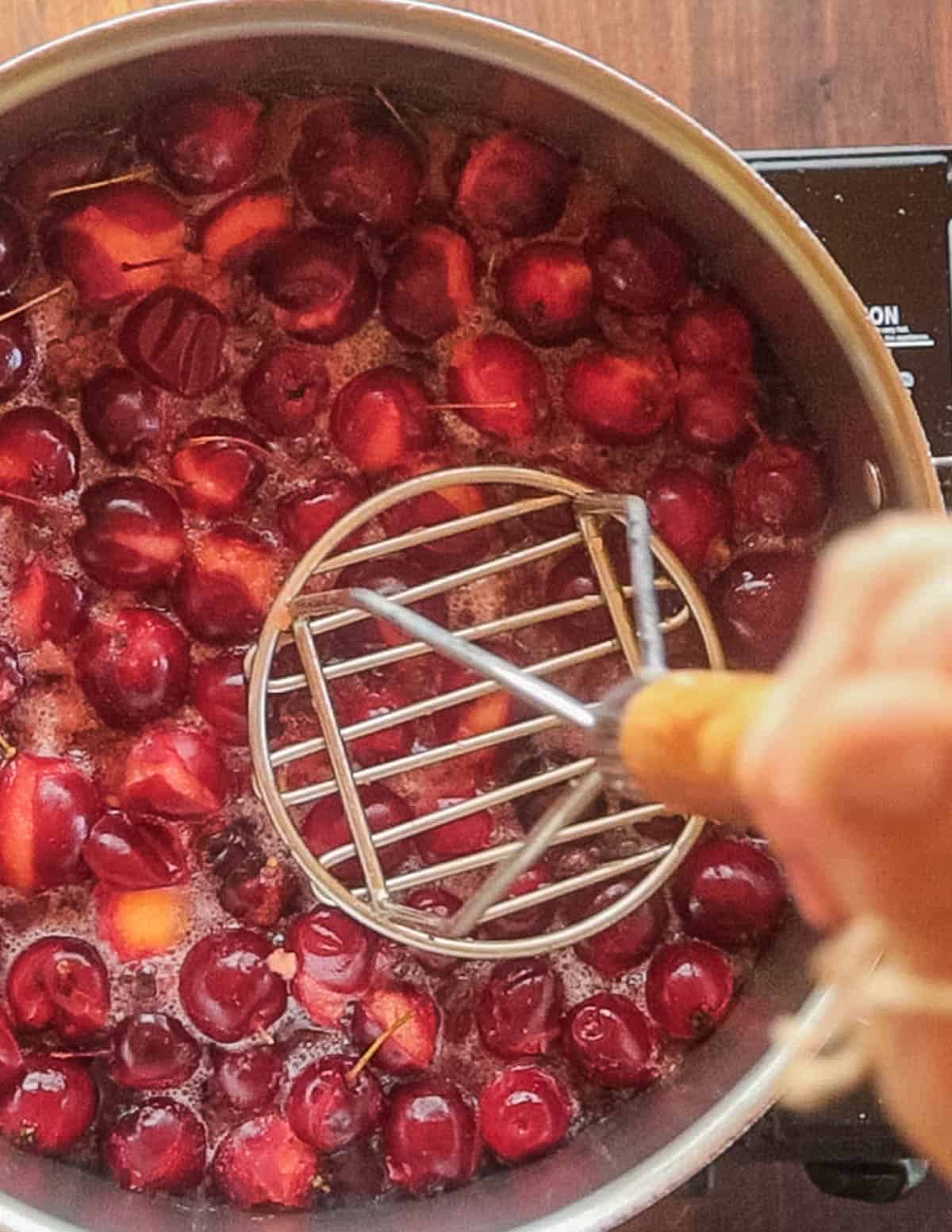 Mashing cooked crab apples with a potato masher. 