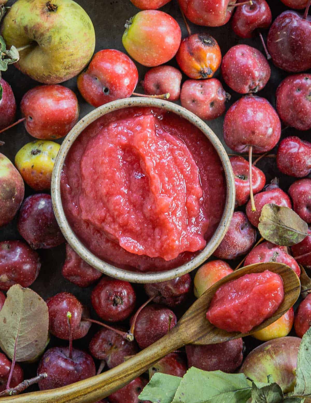 A bowl of pink crabapple sauce next to wild crabapples. 