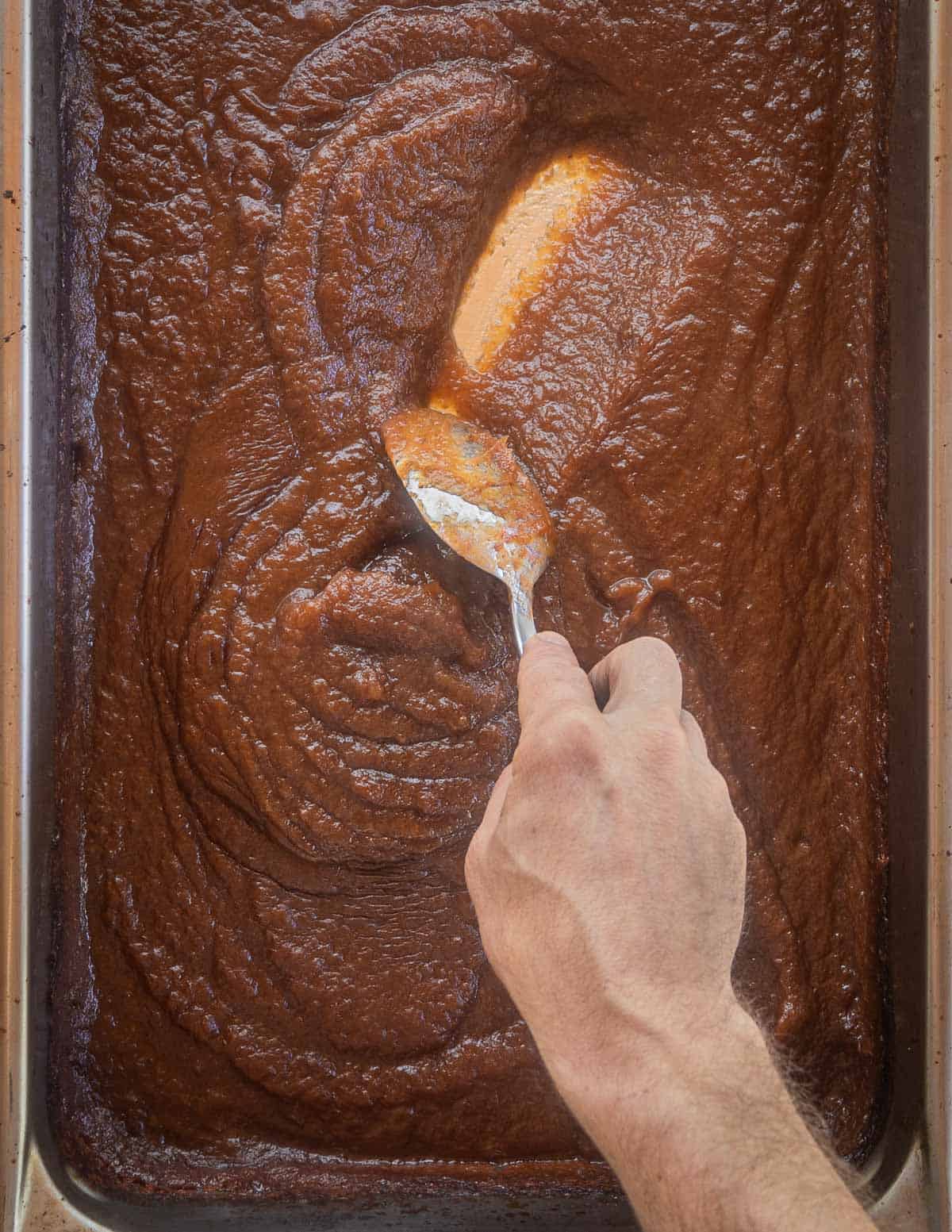 A spoon dragging through a tray of finished apple butter showing evaporation and thickness. 