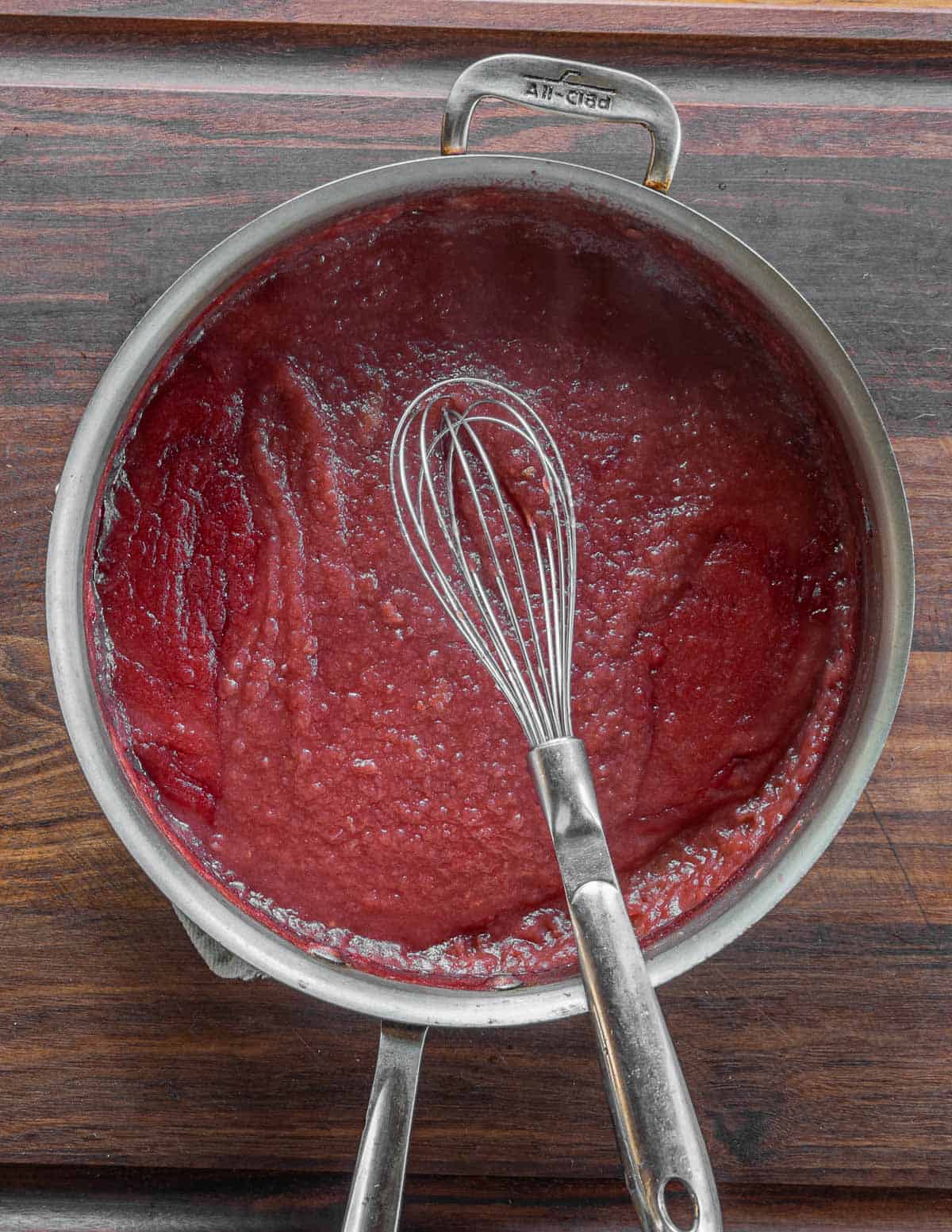 Red crab apple sauce in a pan being whisked. 
