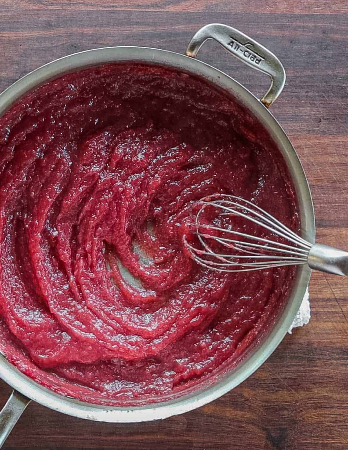 Baked red crab apple butter being whisked in a pan. 