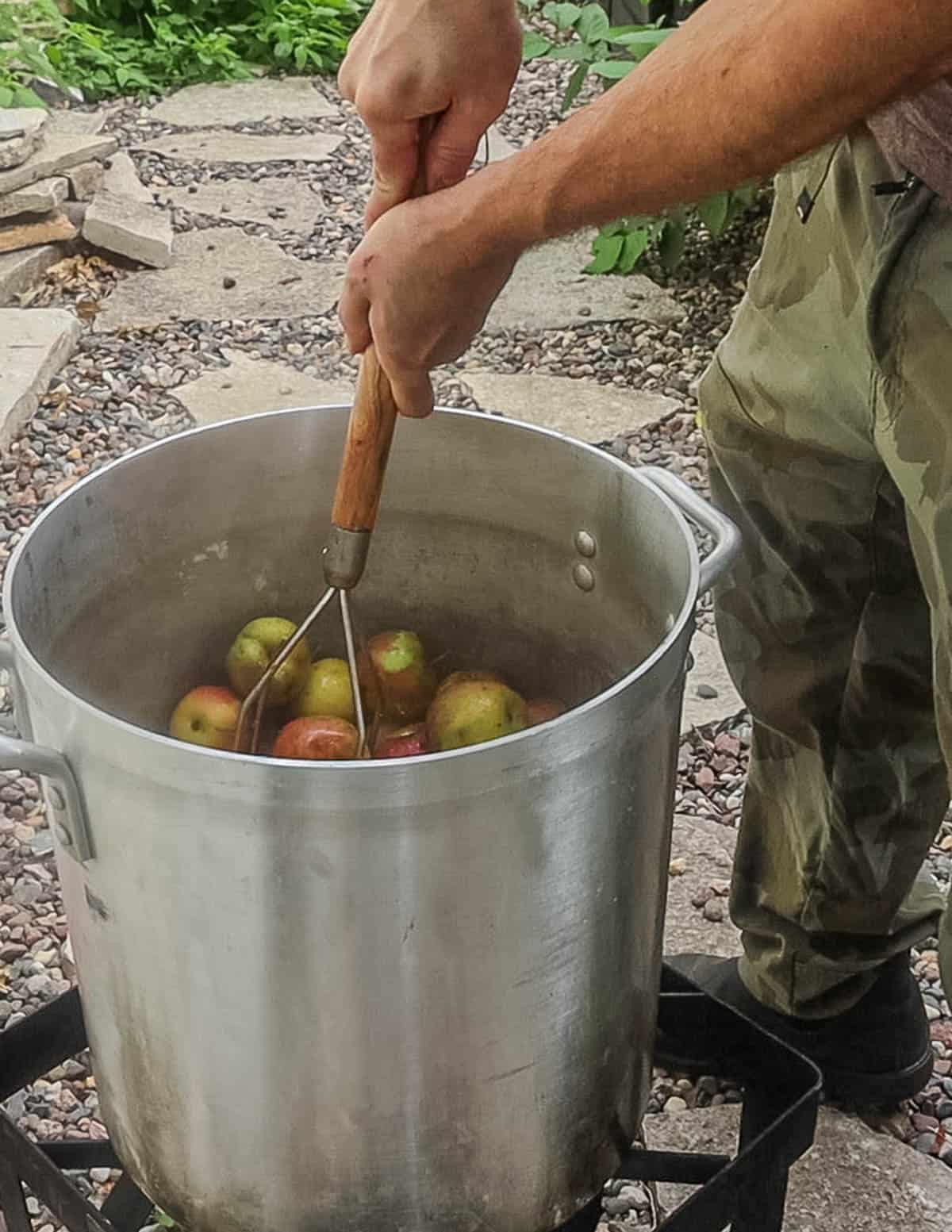 Mashing cooked apples with a potato masher.
