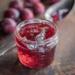 A jar of Dolgo crab apple jelly next to a spoonful of jelly and fresh crab apples.