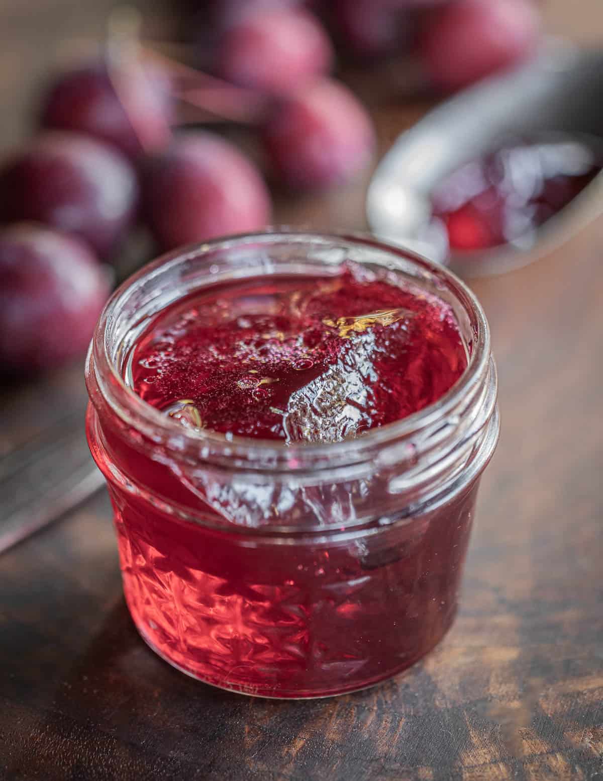 A jar of red crab apple jelly next to red dolgo crab apples. 