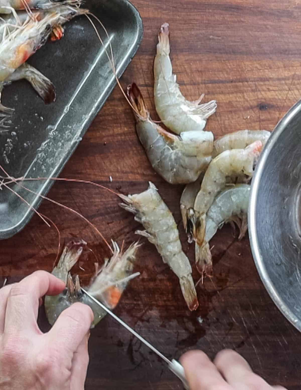 Removing heads from shrimp using a paring knife.