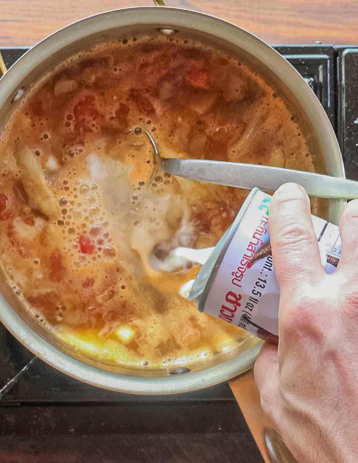 Adding coconut milk to a pot of soup.