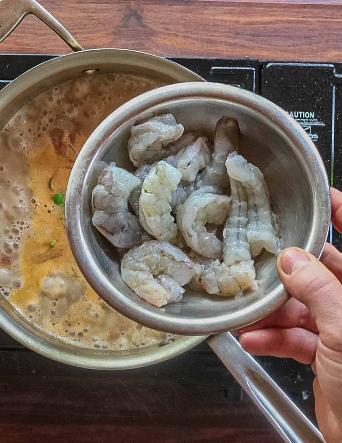 Adding shrimp to a pot of Thai mushroom soup. 