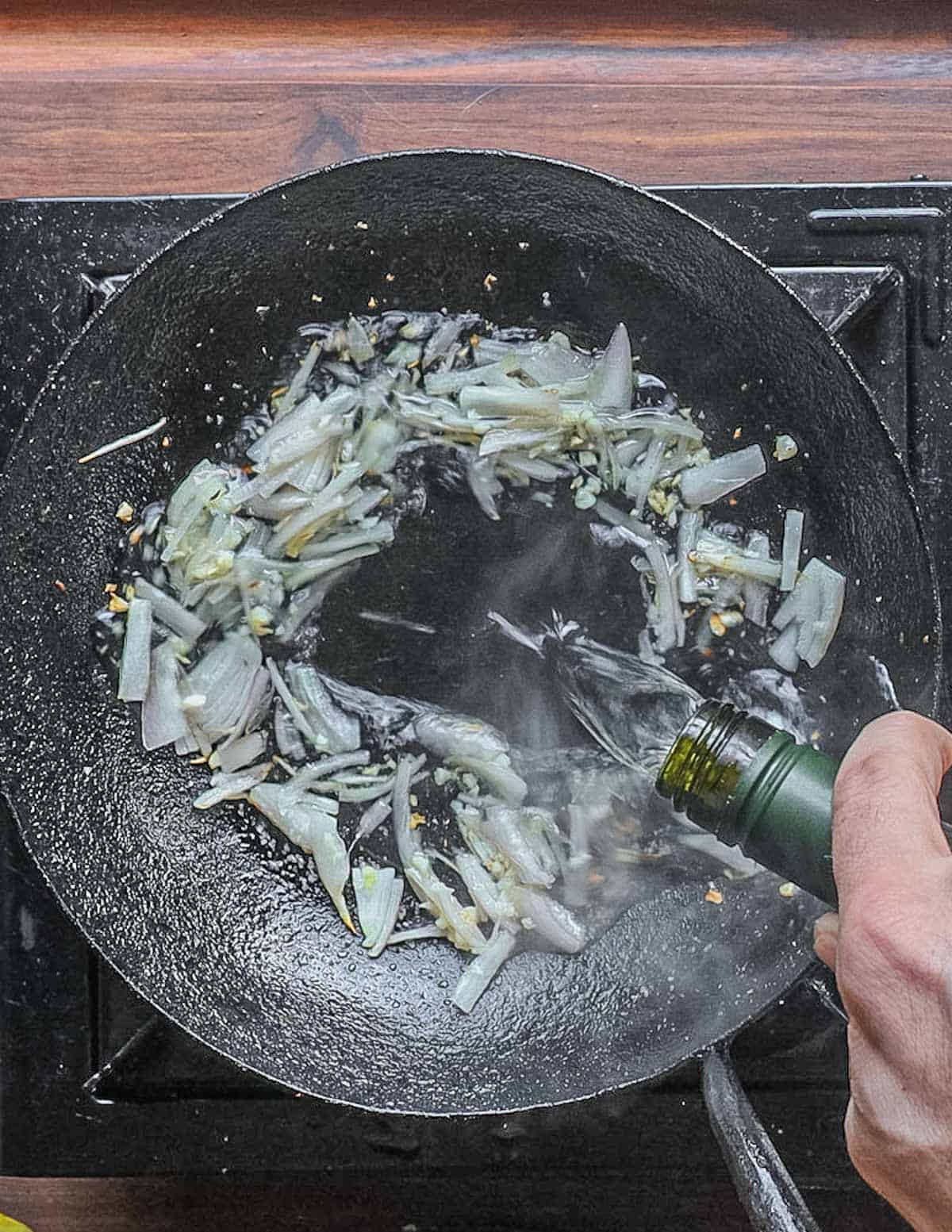 Adding white wine to a pan of cooked garlic and shallots. 
