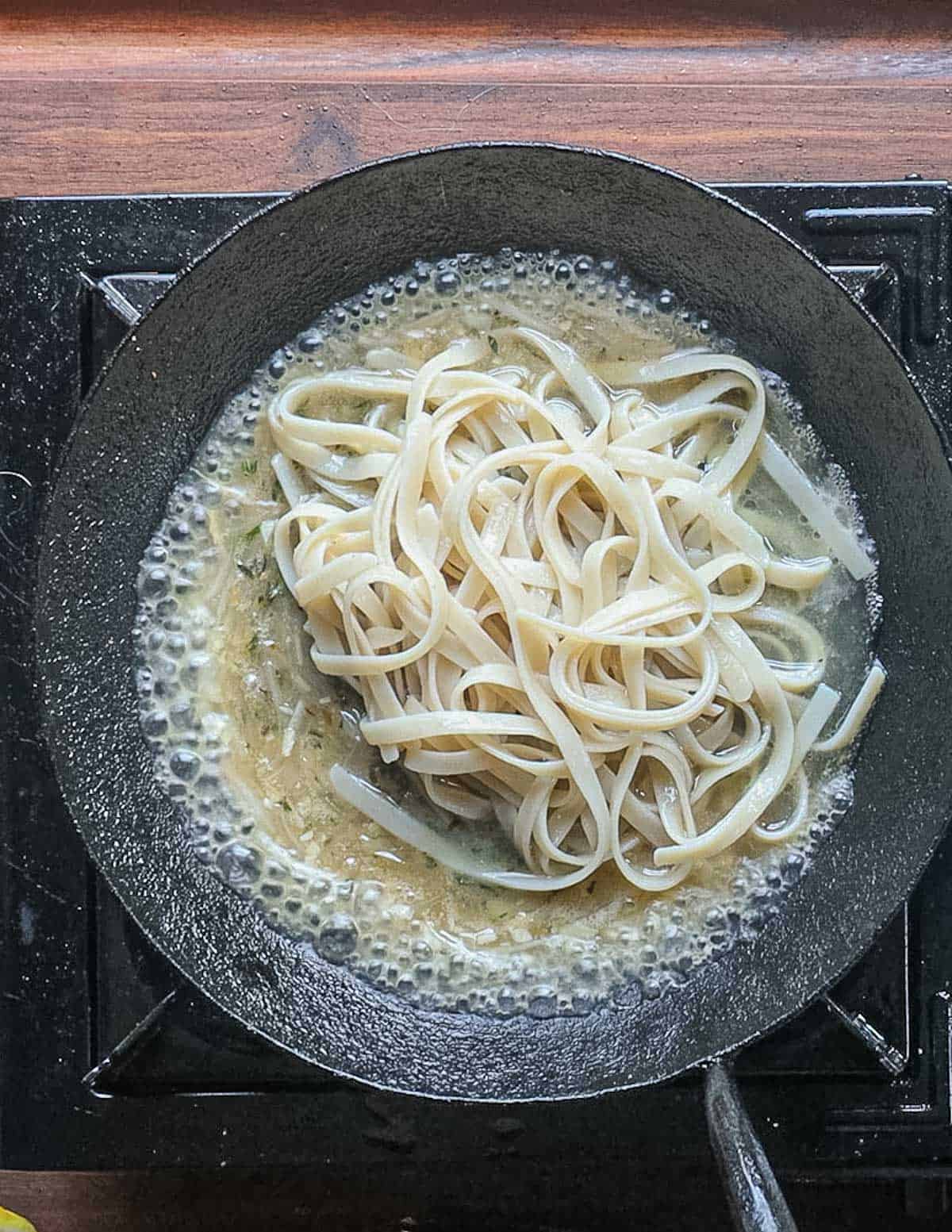 Adding cooked fettucine to a pan. 