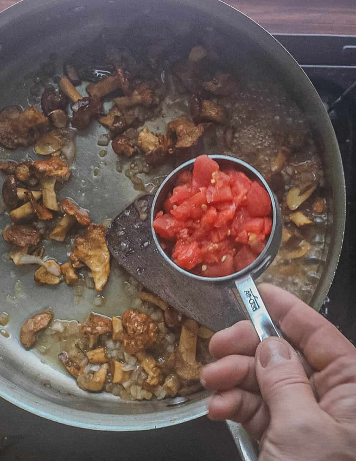 Adding chopped, peeled tomatoes to a pan of cooked mushrooms, shallots and garlic. 