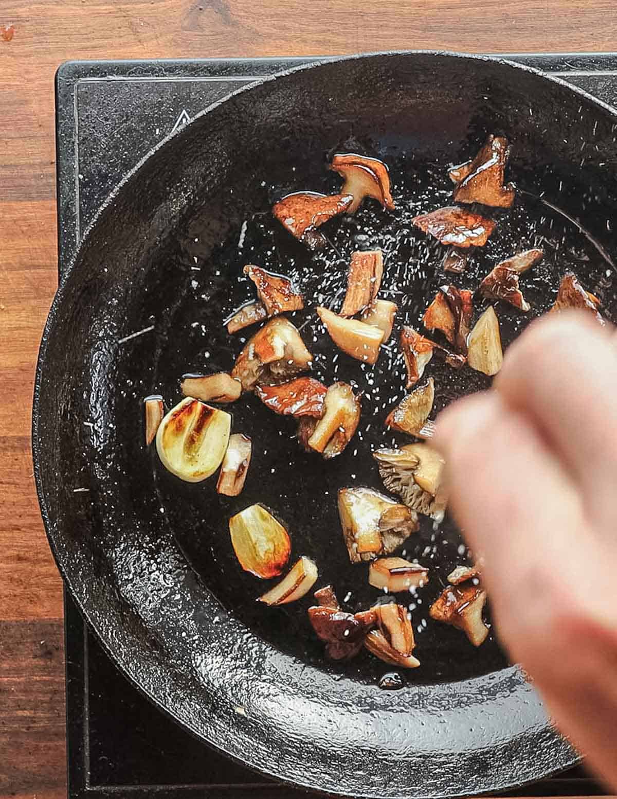 Adding salt to a pan of sauteed mushrooms. 