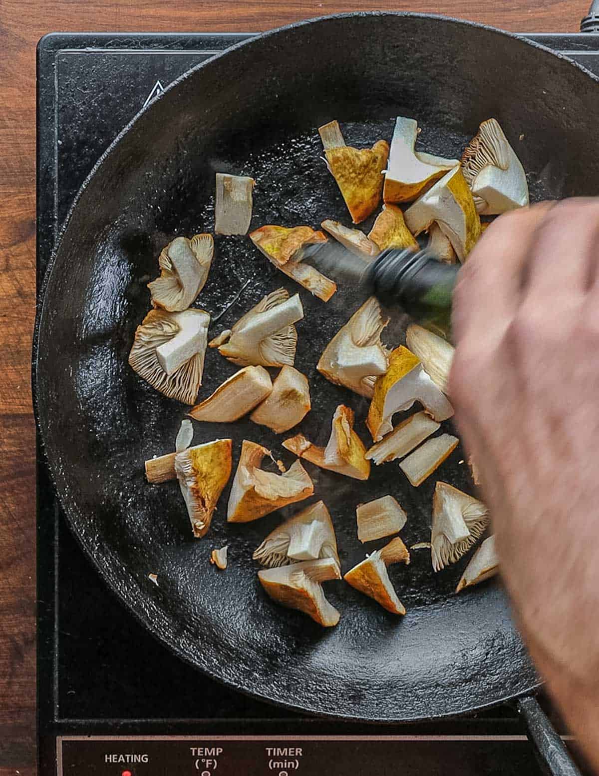 Adding oil to a pan of mushrooms. 