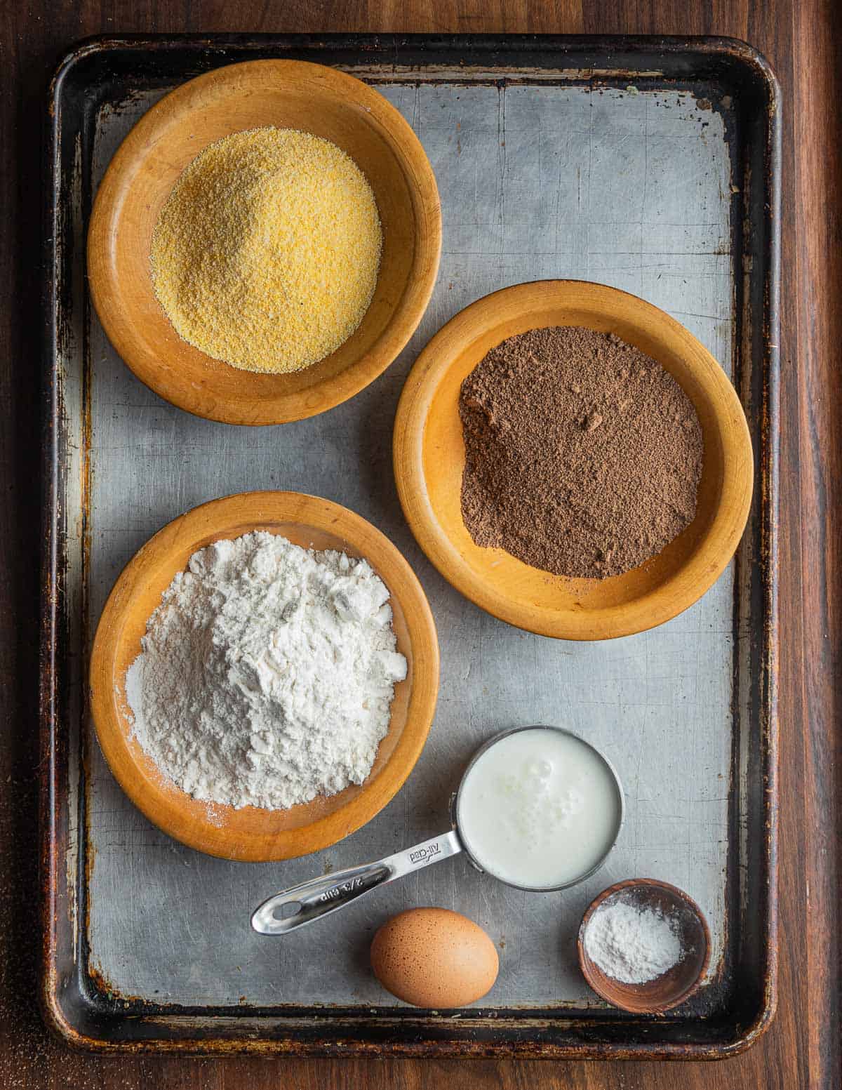 Acorn pancake ingredients laid out on a baking sheet: acorn meal, buttermilk, cornmeal, wheat flour, baking powder, sugar, egg, salt, melted butter. 