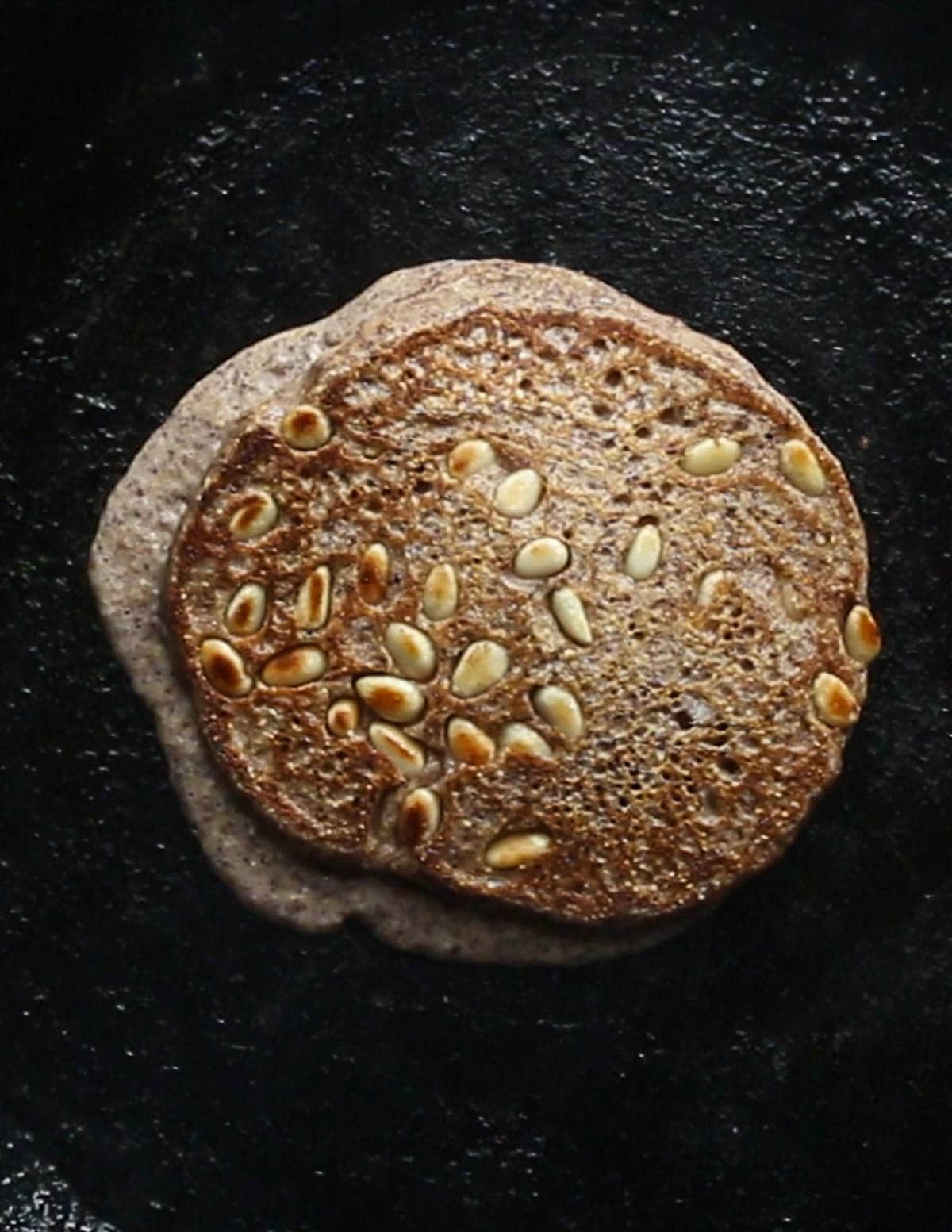 A golden brown, perfectly cooked acorn pancake with pine nuts in it. 