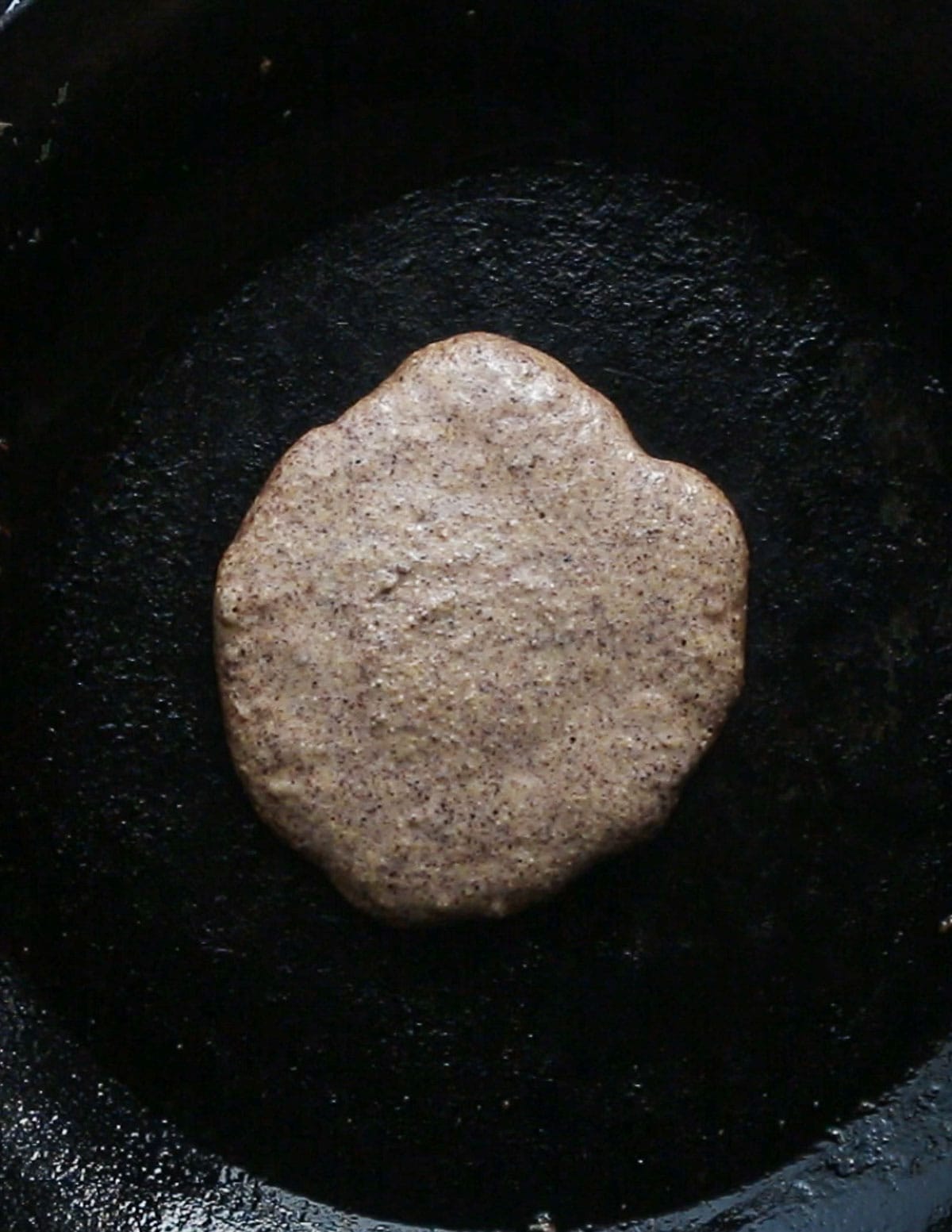 Pouring acorn pancake batter over pine nuts cooking in a pan. 