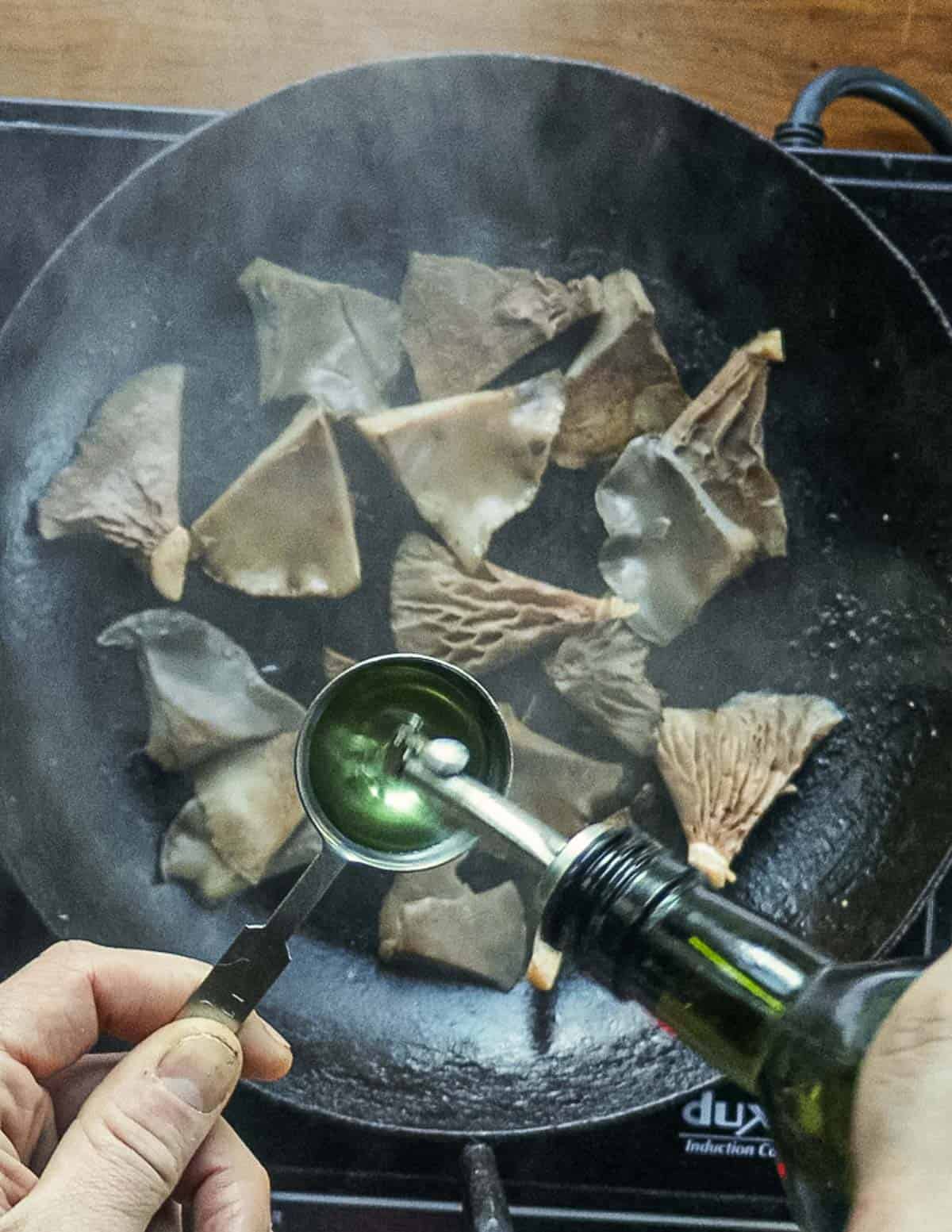 Adding oil to a saute pan of mushrooms. 