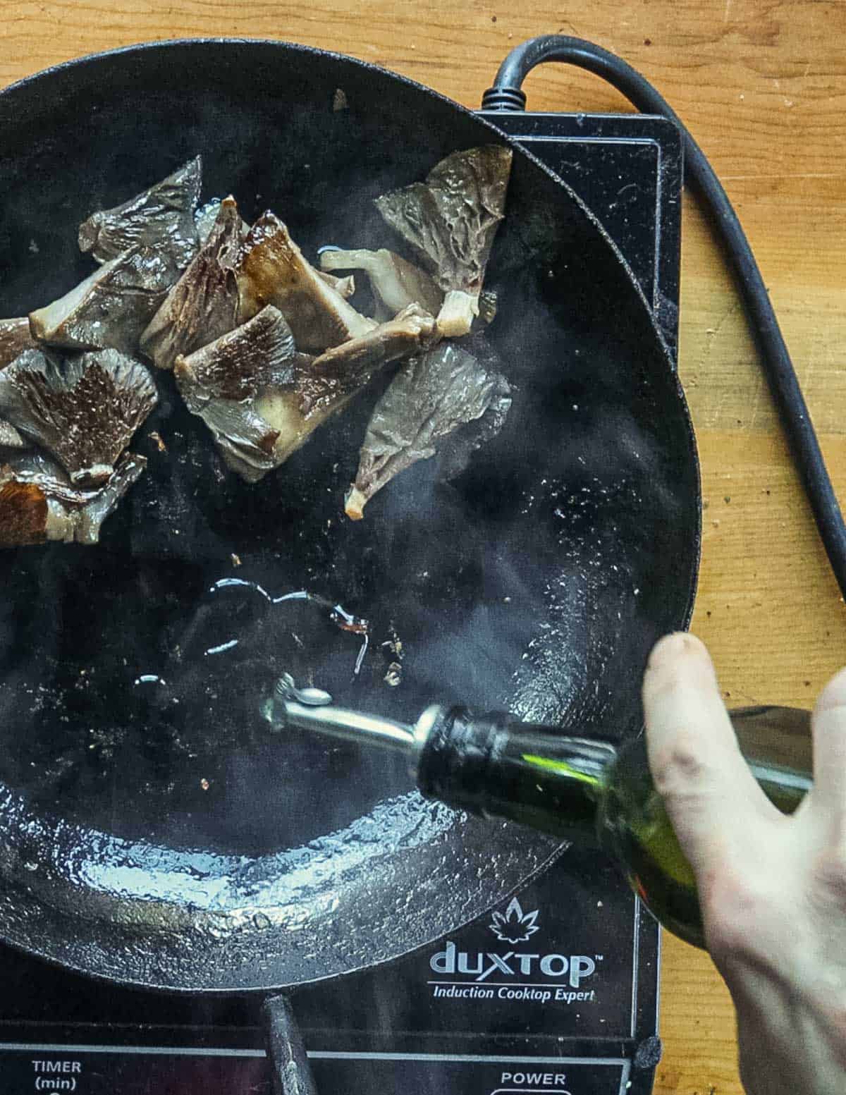 Adding oil to a pan of sauteed mushrooms. 