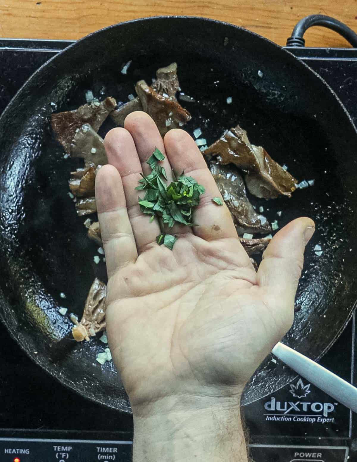 Adding chopped tarragon to a pan of sauteed mushrooms. 