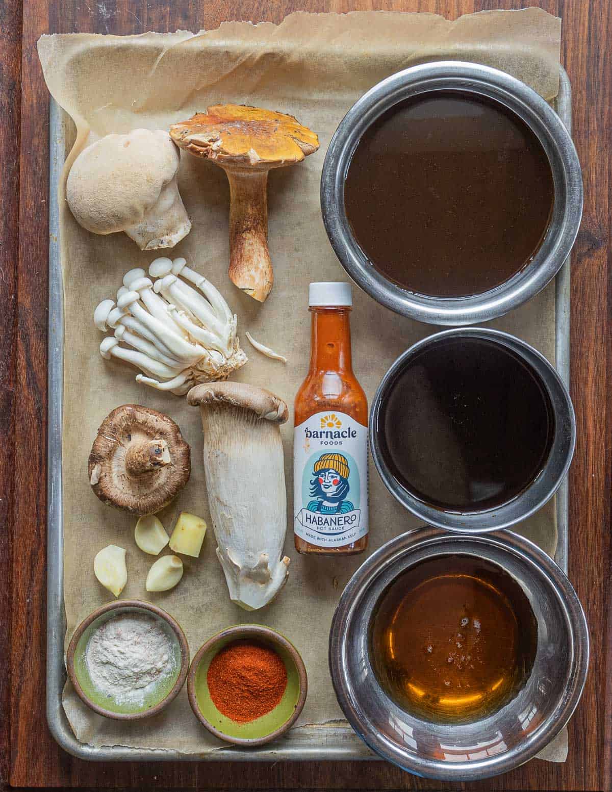 Ingredients for mushroom jerky laid on a tray: maple syrup, soy sauce, hot sauce, onion powder, smoked paprika. 