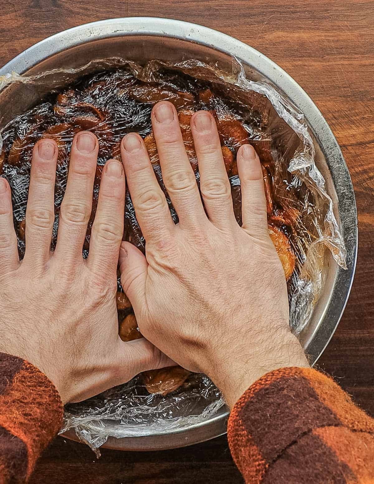 Pressing down on cling film on a bowl of marinating mushrooms. 