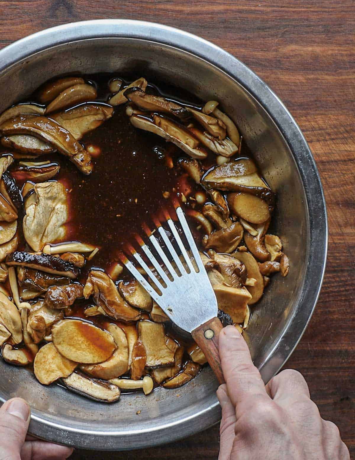 Stirring marinating mushrooms in a bowl using a spatula. 