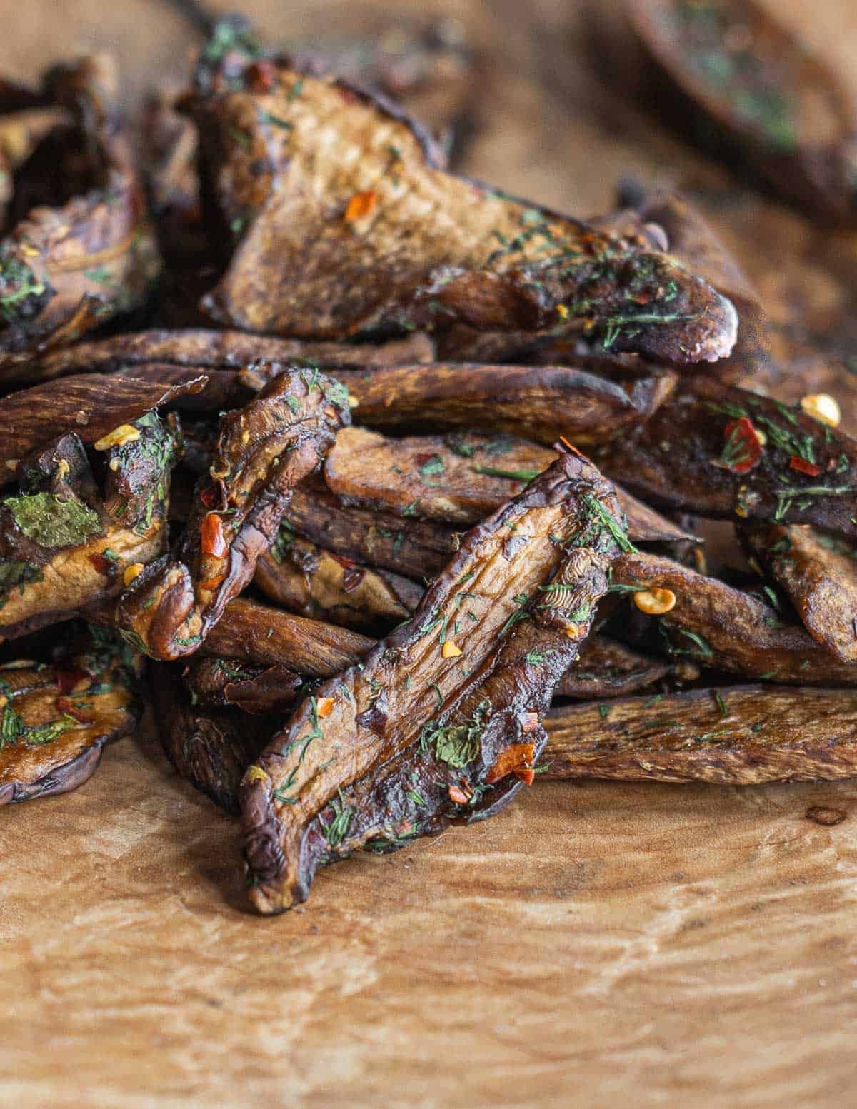 Porcini mushroom jerky with herbs and hot pepper on a wooden tray. 