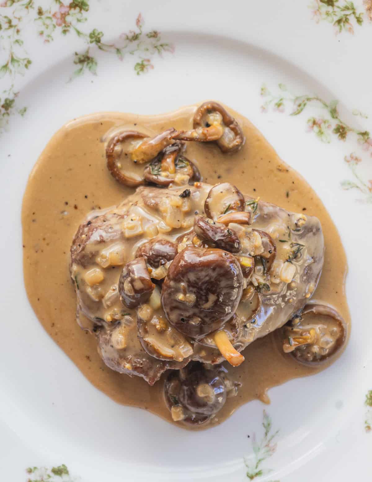 A top down image of a backstrap with mushroom peppercorn sauce on a china plate. 