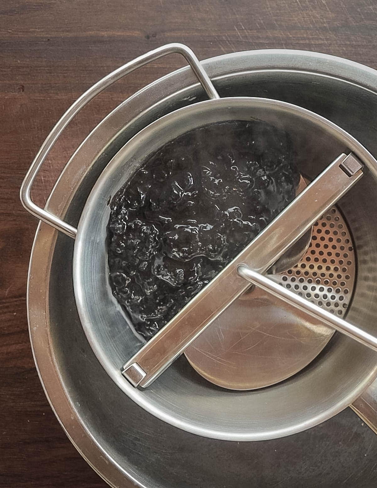 Straining cooked pureed nannyberries through a food mill strainer. 