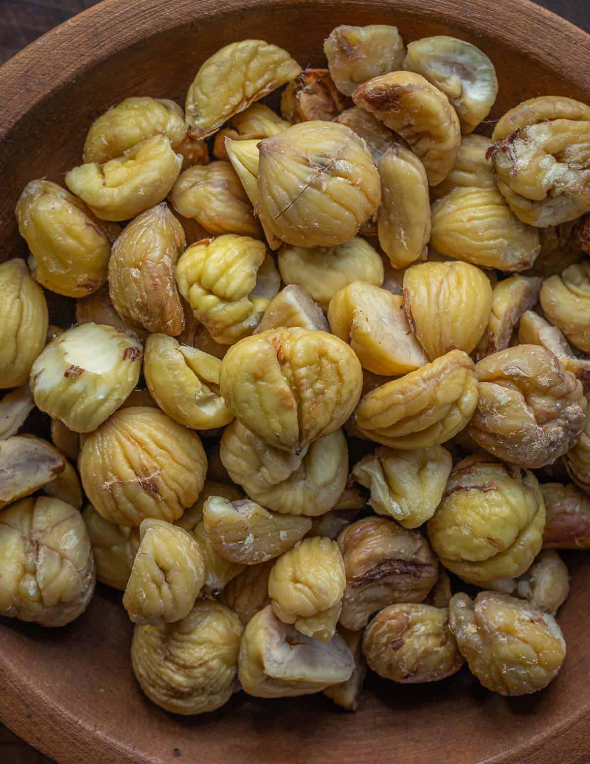 A close up image of a wooden bowl filled with freshly cooked chestnuts.