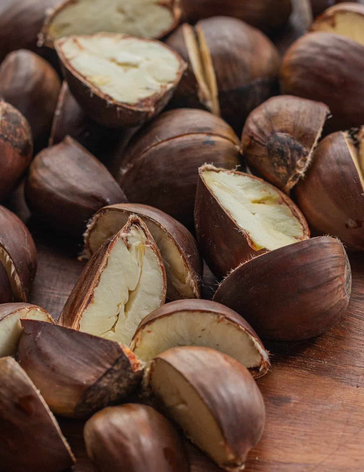 A close up image of fresh chestnuts cut in half on a cutting board before steaming. 