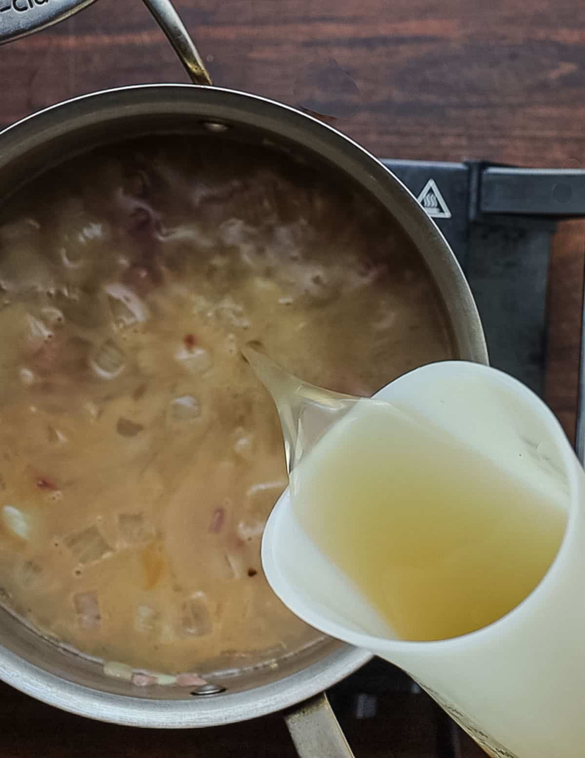 Adding chicken stock to a soup pot of cooked onions.