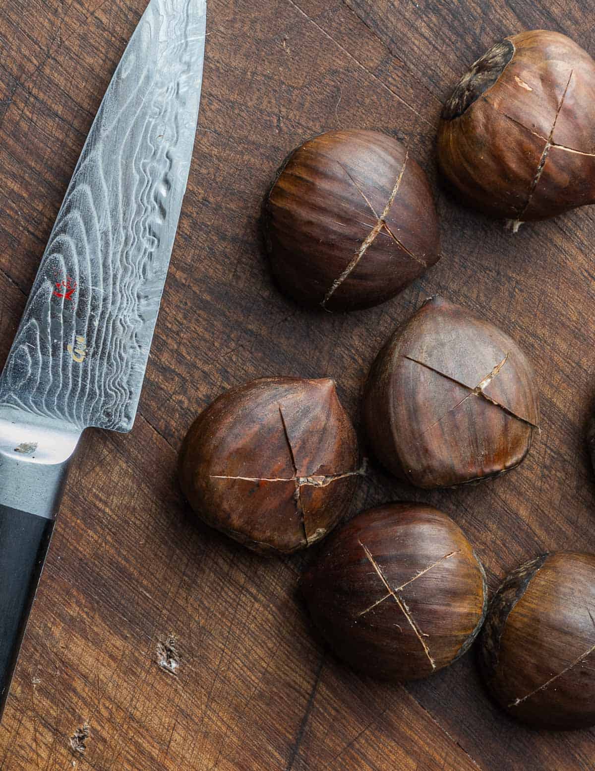 Italian chestnuts that have been scored with a knife on a cutting board.